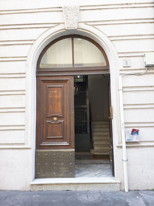 A wooden door with a brass handle and a metal plate, set in a white building with a stone base and a small window above the door.