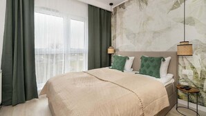 Un dormitorio con una cama grande, cortinas verdes, un mural en la pared y dos lámparas colgantes.