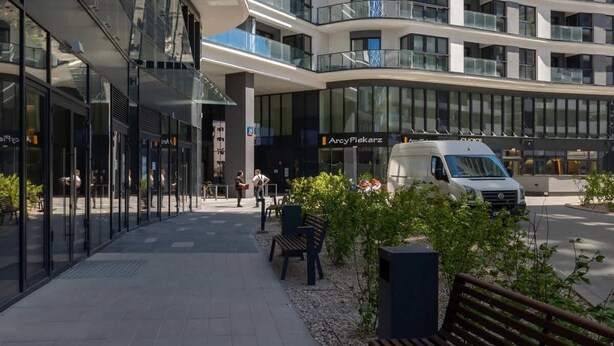 A modern high-rise building with a curved facade, large windows, and a visible entrance with a sign. - Stylish Apartment in Wola | Balcony and Air Conditioning (Warszawa)