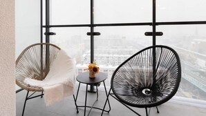A high-rise room with large windows, two wicker chairs, a small round table with a vase of flowers, and a cityscape view. - Stylish Apartment in Wola | Balcony and Air Conditioning (Warszawa)