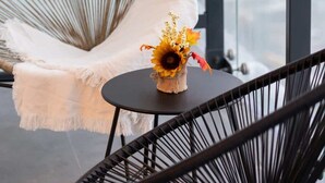 A wicker chair with a white cushion and a small table with a vase of flowers. - Stylish Apartment in Wola | Balcony and Air Conditioning (Warszawa)
