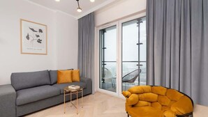 A modern living room with a grey sofa, a small wooden side table, a yellow armchair, and a large window with grey curtains. - Stylish Apartment in Wola | Balcony and Air Conditioning (Warszawa)