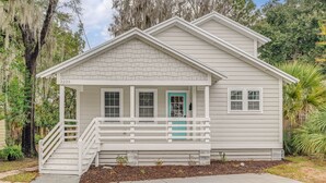 A single-story house with a white exterior, a front porch with white railings, and a turquoise door. - 3BR Home | Near Savannah and Marina + Workspace (Savannah)