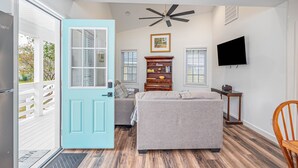 A modern living room with a teal door, a ceiling fan, a TV, a sofa, a cabinet, and a window. - 3BR Home | Near Savannah and Marina + Workspace (Savannah)