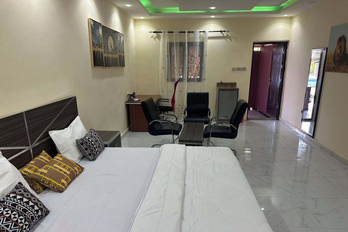 A hotel room with a large bed, a desk, two chairs, a small table, and a window with curtains.