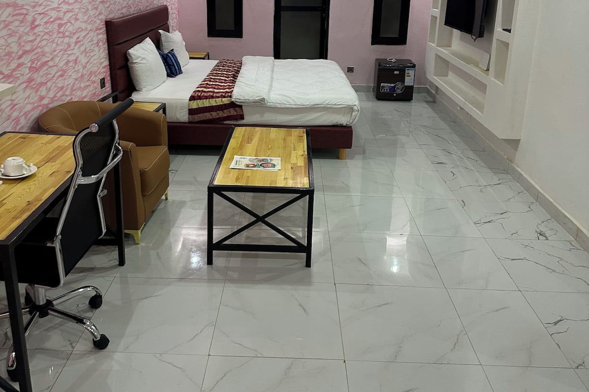 A hotel room with a bed, a desk, a chair, a TV, and an air conditioning unit.