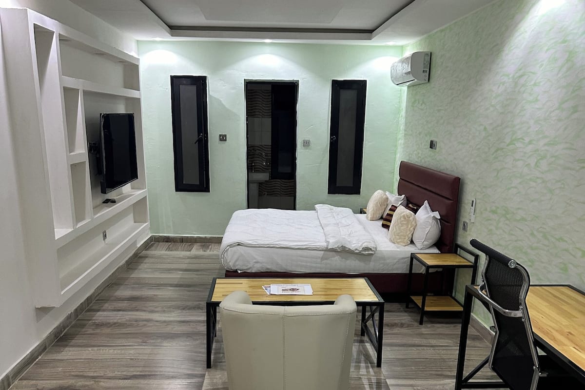 A modern bedroom with a bed, a desk, a chair, and a TV.