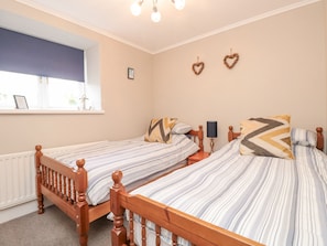 A bedroom with two single beds, a window, a radiator, and a wall-mounted lamp.