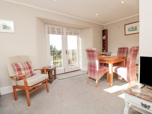 A living room with a wooden dining table, plaid chairs, a sofa, and a television.