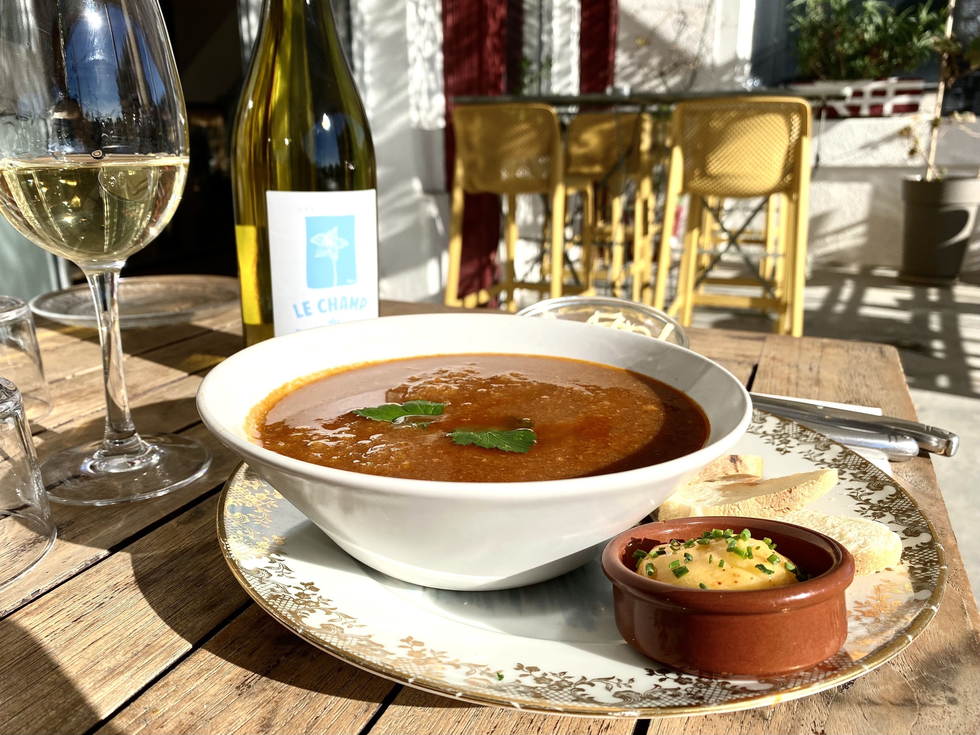 Una mesa con un tazón de sopa, un recipiente pequeño de mostaza y una botella de vino.