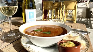 Una mesa con un tazón de sopa, un recipiente pequeño de mostaza y una botella de vino.