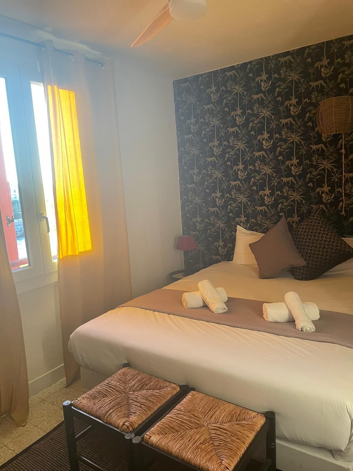 Habitación de hotel con una cama, dos almohadas, una mesita de noche, una lámpara y una ventana con cortinas.