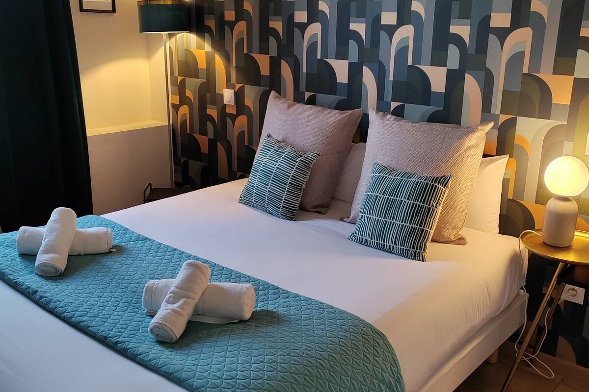 A neatly made bed with a teal quilt, white linens, and multiple pillows.