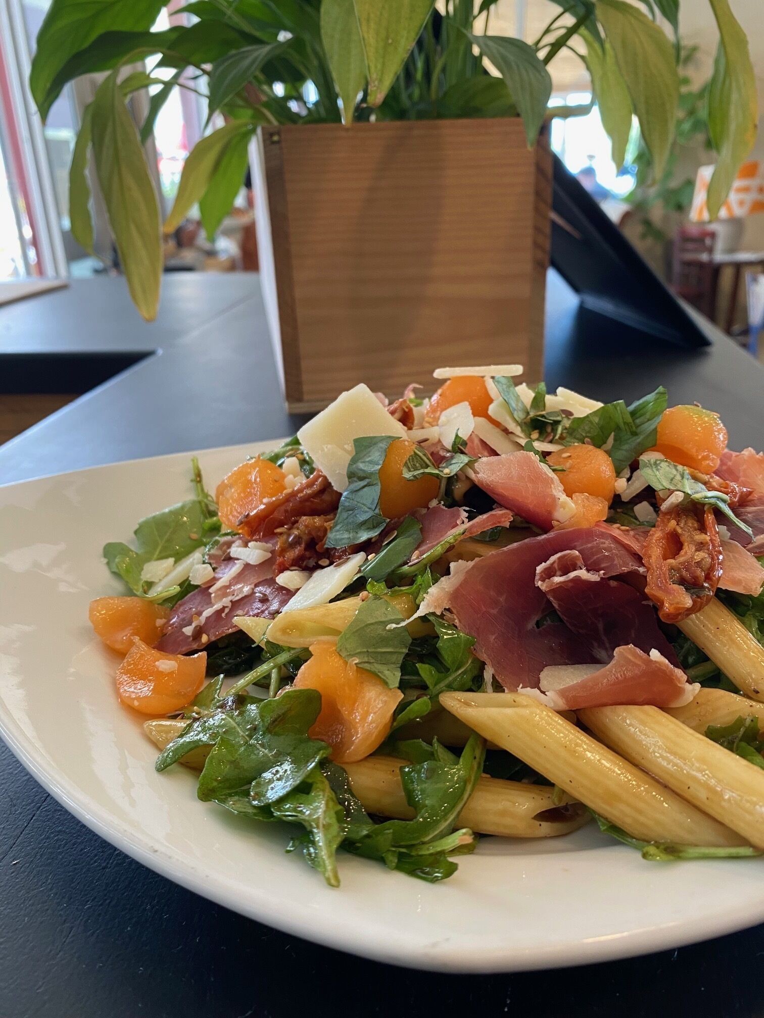 Een bord pasta salade met groenten, sinaasappelpartjes en parmaham.