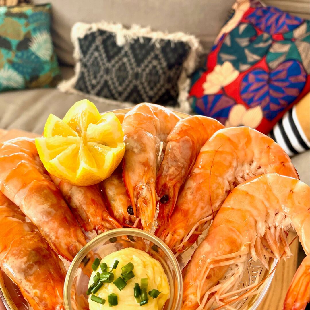 A platter of cooked shrimp with lemon slices and a small bowl of butter.