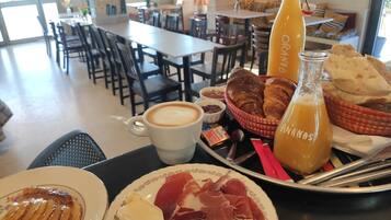 Un esmorzar amb croissants, suc d'aranja, cafè, formatge i embutits sobre un safata.