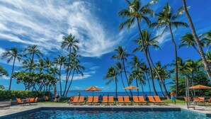 A poolside area with lounge chairs and umbrellas, palm trees, and a view of the ocean. - Exquisite Prime Beachfront Haven, Indulge in Tropical Luxury -Wailea Elua 1302 (Wailea, Maui)