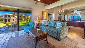 A spacious living area with a ceiling fan, a sofa, a glass coffee table, and a view of the outdoors. - Exquisite Prime Beachfront Haven, Indulge in Tropical Luxury -Wailea Elua 1302 (Wailea, Maui)