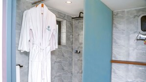 Une salle de bain carrelée de marbre, une robe blanche suspendue à un porte-serviettes et un espace douche.