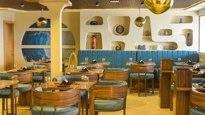 L’intérieur d’un restaurant est aménagé avec des meubles en bois, des sièges rembourrés de couleur bleue et des œuvres d’art décoratives sur les murs.