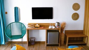Un espace de vie compact comprenant un canapé, un fauteuil, une petite table avec une bouilloire et un téléviseur fixé au mur.