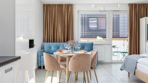 A modern, well-lit room with a dining table set for two, a blue sofa, and a bed with a grey blanket. - Seaside Apartamenty Kasprowicza 14  (Kolobrzeg)