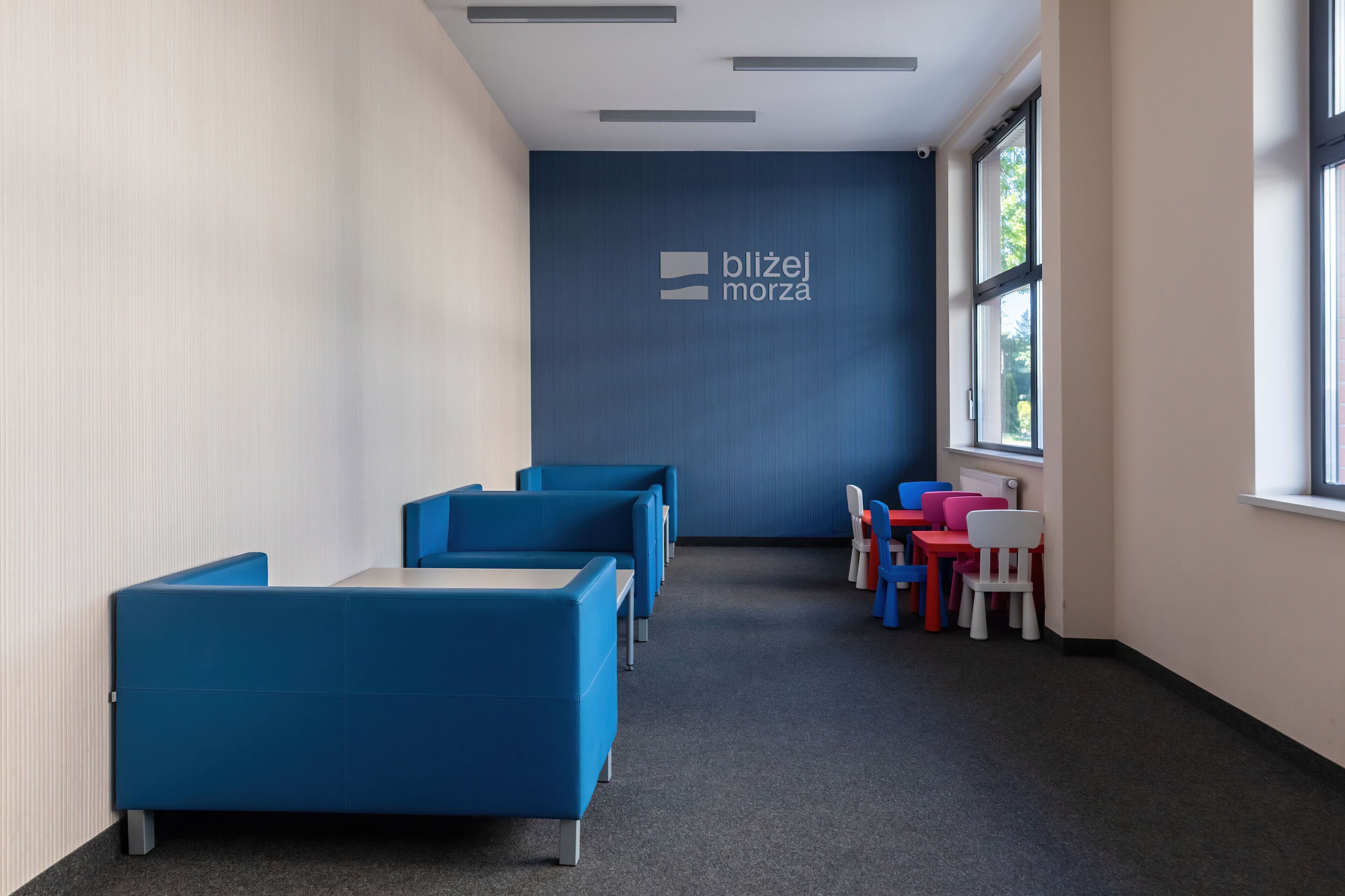 Un área de espera moderna con asientos azules y una pared azul con el logo 'blijej morza'.