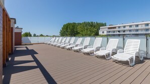 A sun deck with rows of white lounge chairs and a wooden deck floor. - Seaside Apartamenty Kasprowicza 14  (Kolobrzeg)