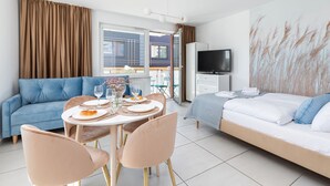 A modern hotel room with a sofa, a dining table set for two, a TV, and a large window with curtains. - Seaside Apartamenty Kasprowicza 14  (Kolobrzeg)