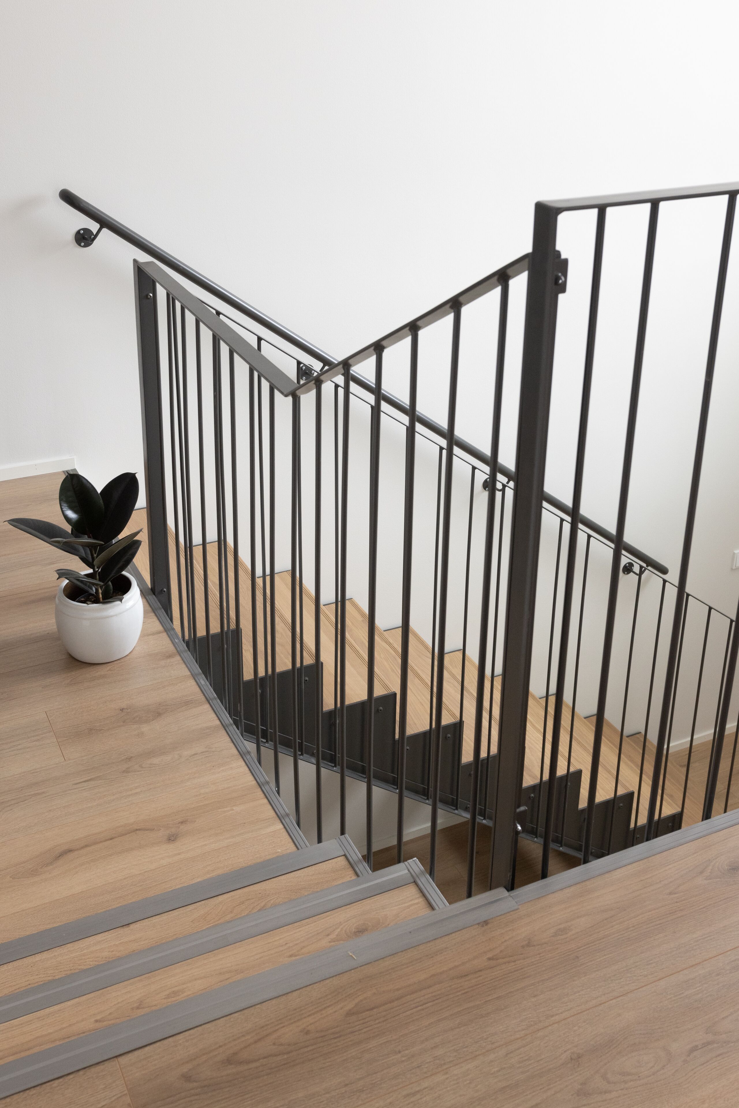 Una escalera con barandilla de metal, escalones de madera y una planta en el rellano.