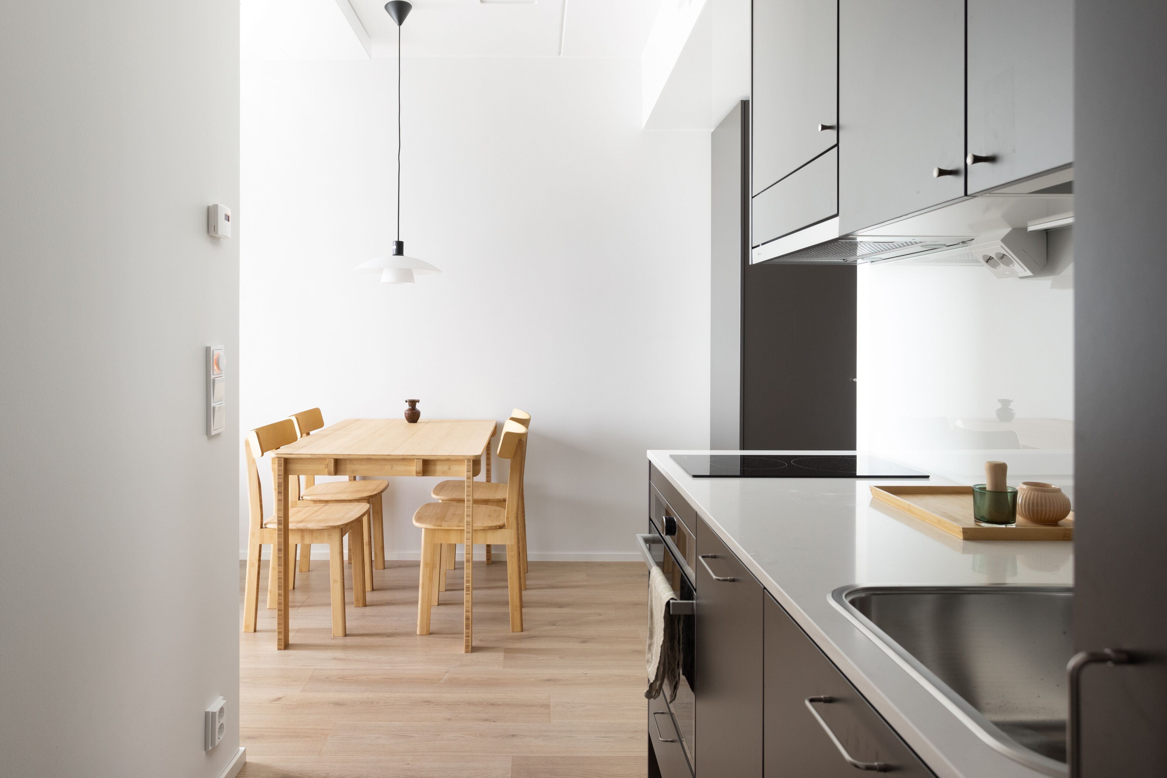 A modern kitchen with a wooden dining table and chairs, a built-in oven, and a stainless steel sink.