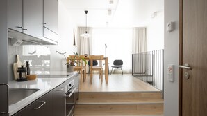 A modern kitchen with stainless steel appliances, wooden dining table, and a staircase leading to a balcony. - Noli Otaniemi (Espoo)