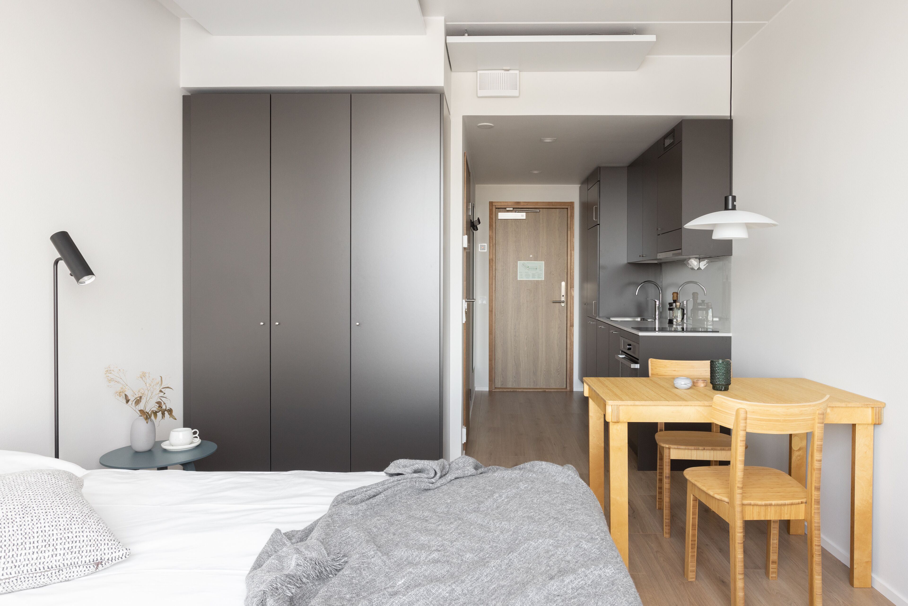 Une chambre à coucher moderne avec un lit, une table de chevet et une petite table sur laquelle se trouvent un vase et une tasse.