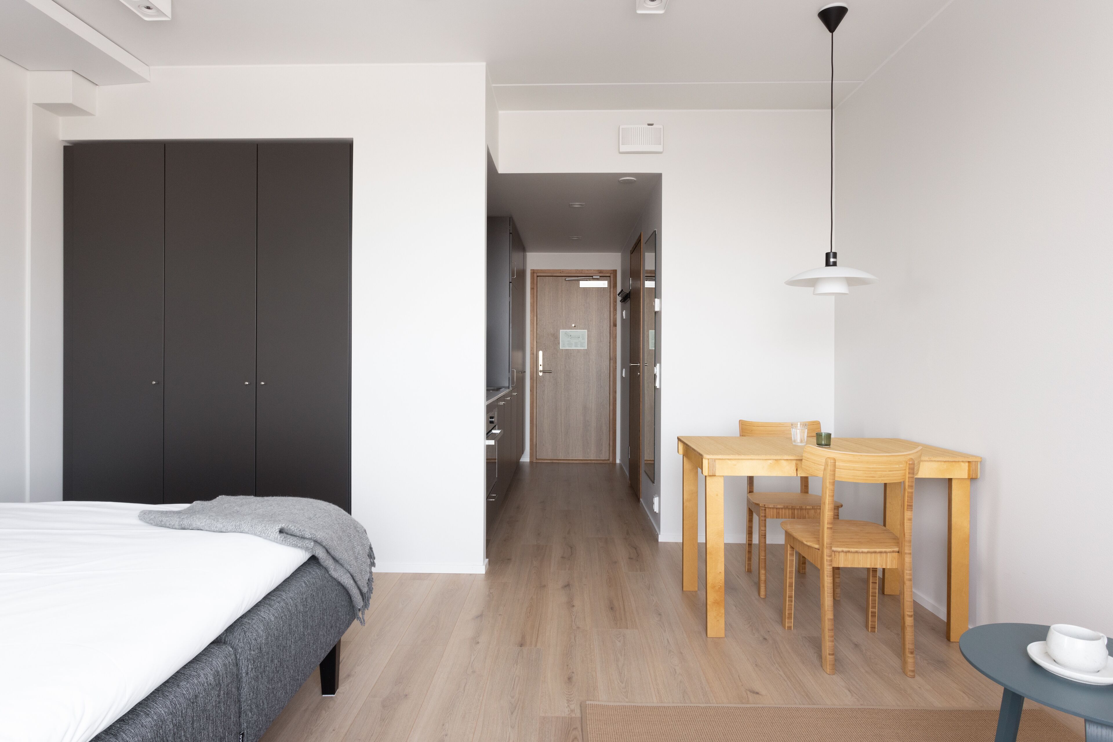 A bedroom with a bed, a wooden table with chairs, a small table with a cup, and a wardrobe.