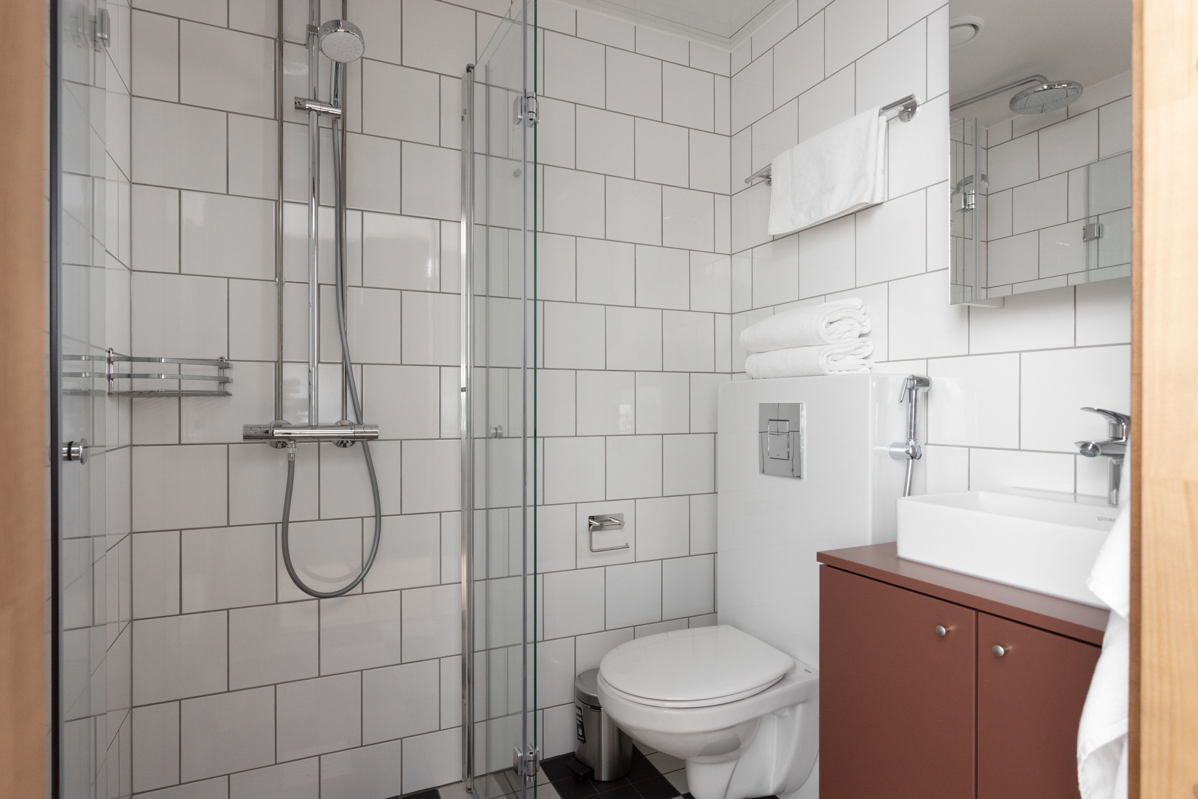 A modern bathroom with a glass-enclosed shower, a white toilet, and a brown vanity with a sink.