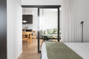A modern hotel room with a bed, a dining area with a table and chairs, a sofa, and a sliding door leading to a balcony. - Noli Otaniemi (Espoo)