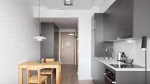 A compact kitchen with modern appliances, a dining area with a wooden table and chairs, and a visible door leading to another room. - Noli Otaniemi (Espoo)
