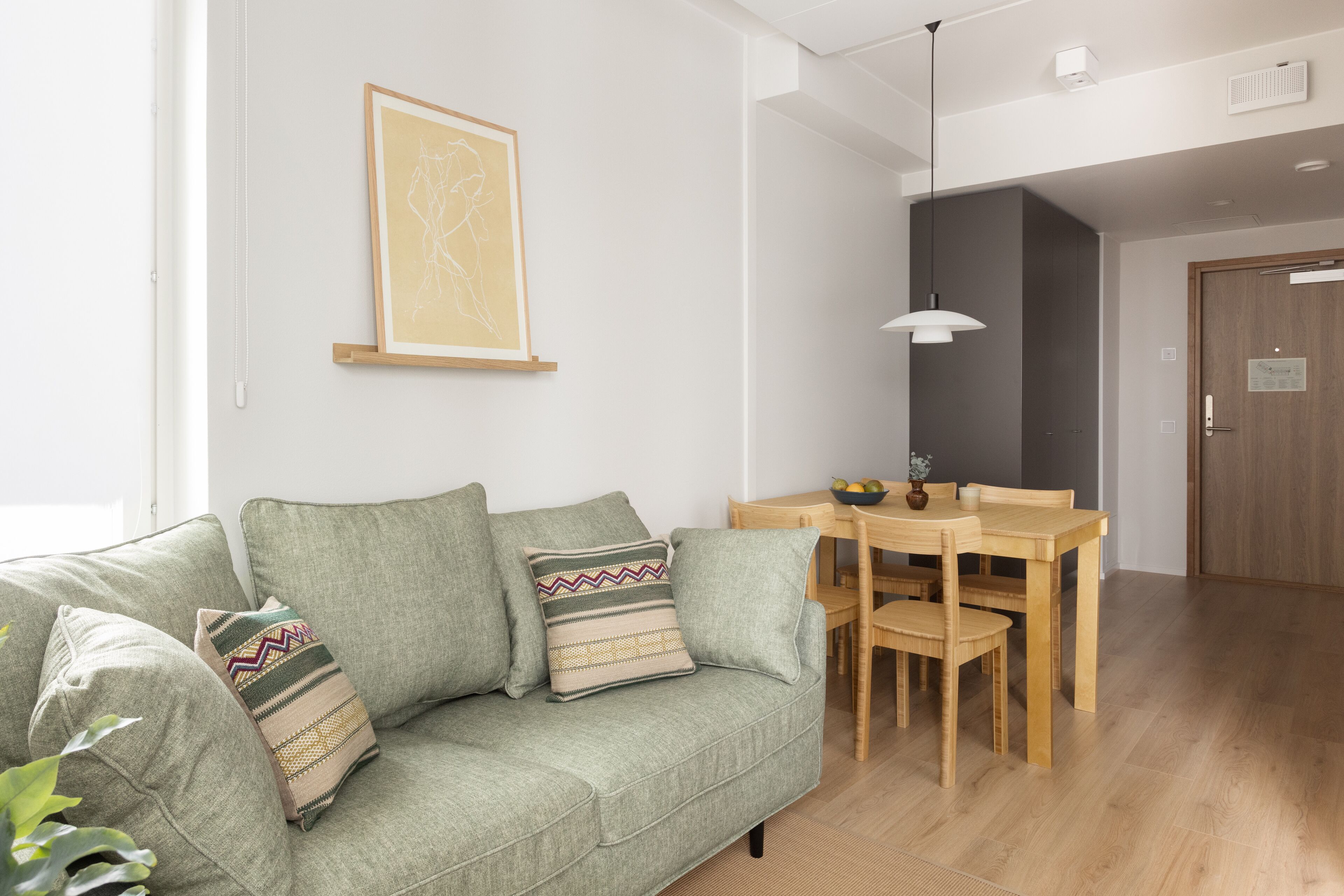 Un salon avec un canapé vert, une table à manger avec des chaises, un luminaire suspendu et un tableau encadré au mur.