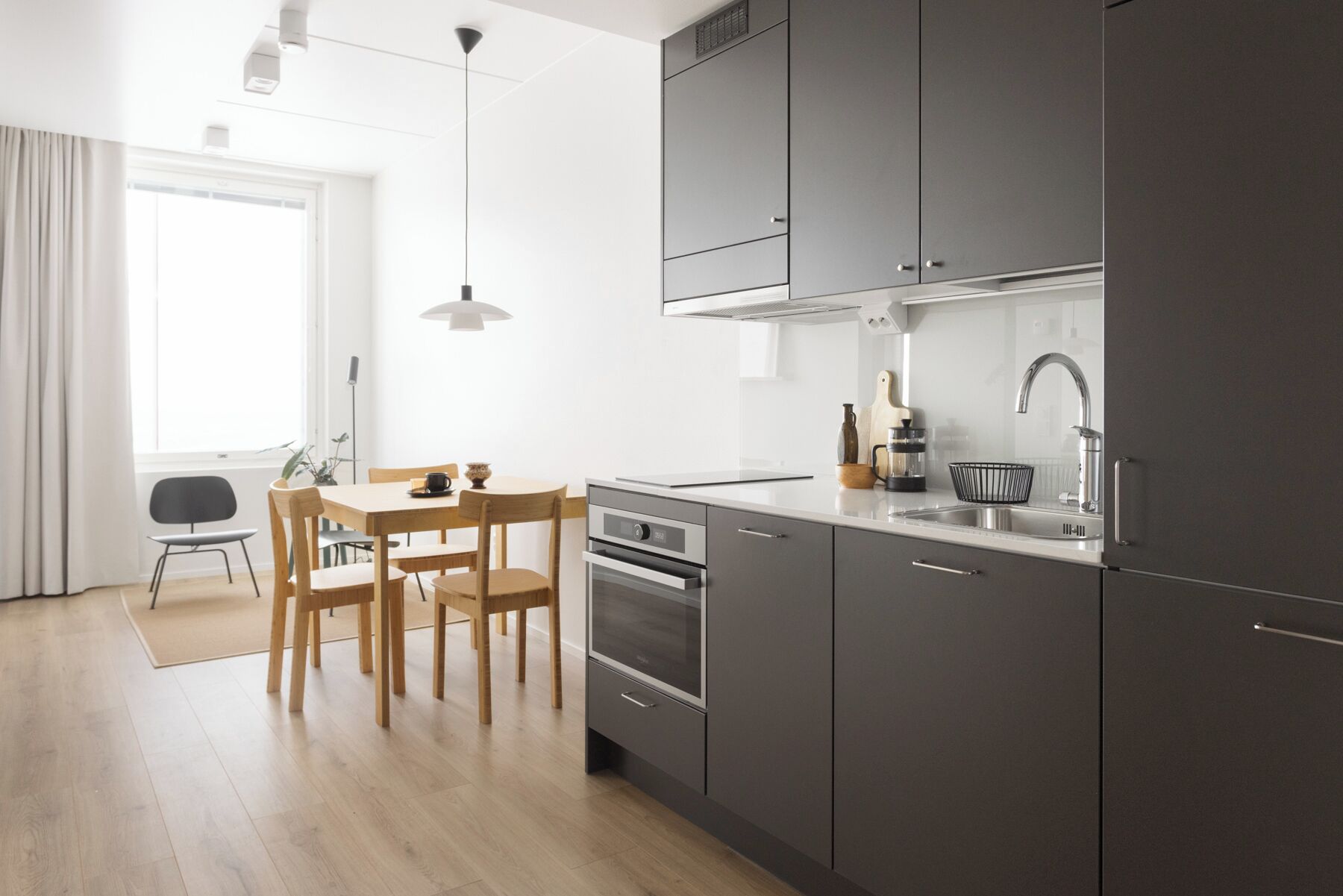 Una cocina moderna con armarios grises, un lavamanos de acero inoxidable y una zona de comedor con mesa y sillas de madera.