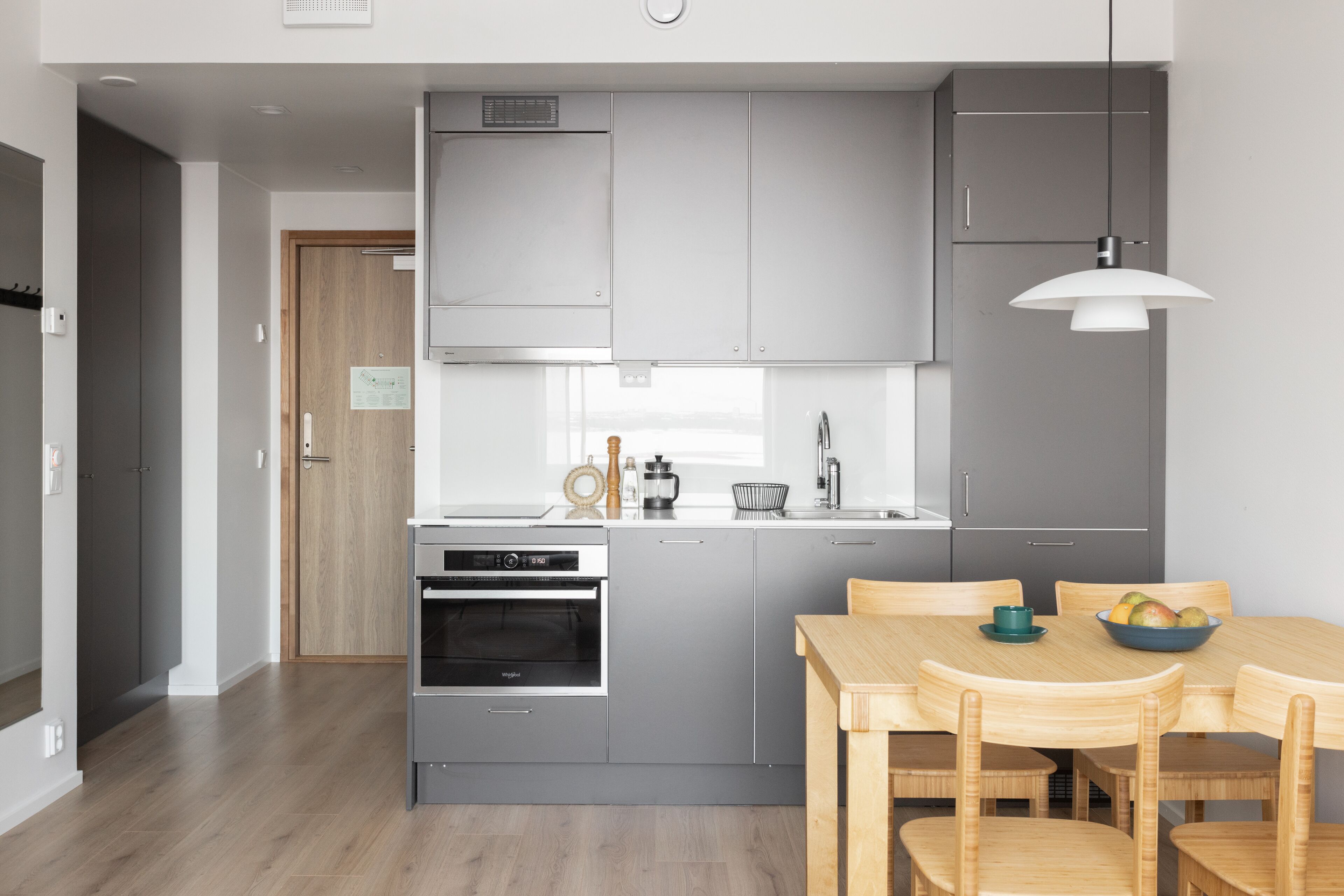 A modern kitchen with grey cabinets, a built-in oven, and a dining area with a wooden table and chairs.