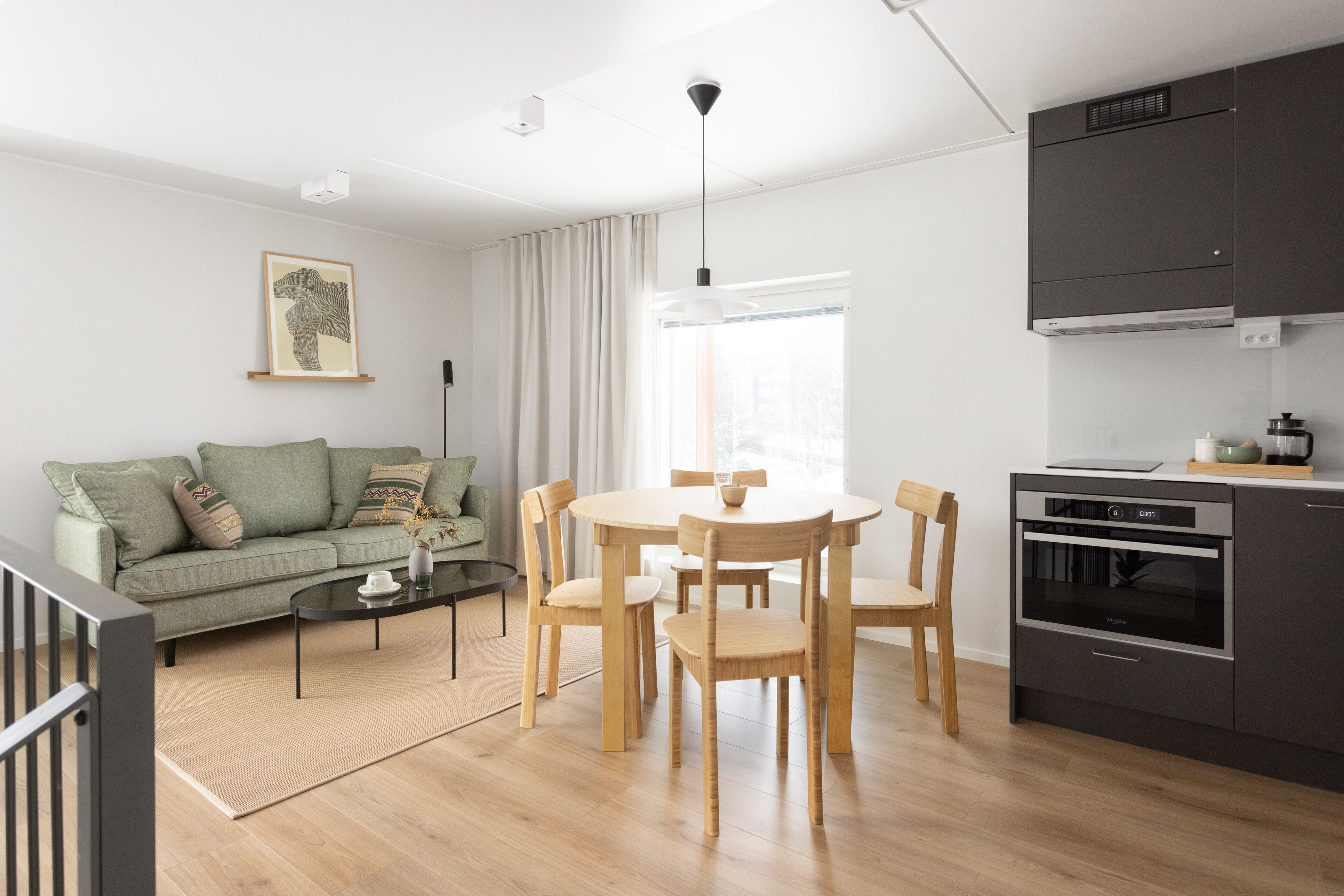 A modern living room with a sofa, coffee table, and dining table with chairs. There is a kitchen area with a stove and cabinets.