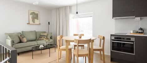 A modern living room with a sofa, coffee table, and dining table with chairs. There is a kitchen area with a stove and cabinets.