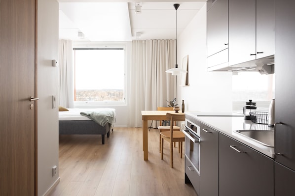 A modern kitchen with a dining area, wooden flooring, and a large window with curtains. - Noli Otaniemi (Espoo)