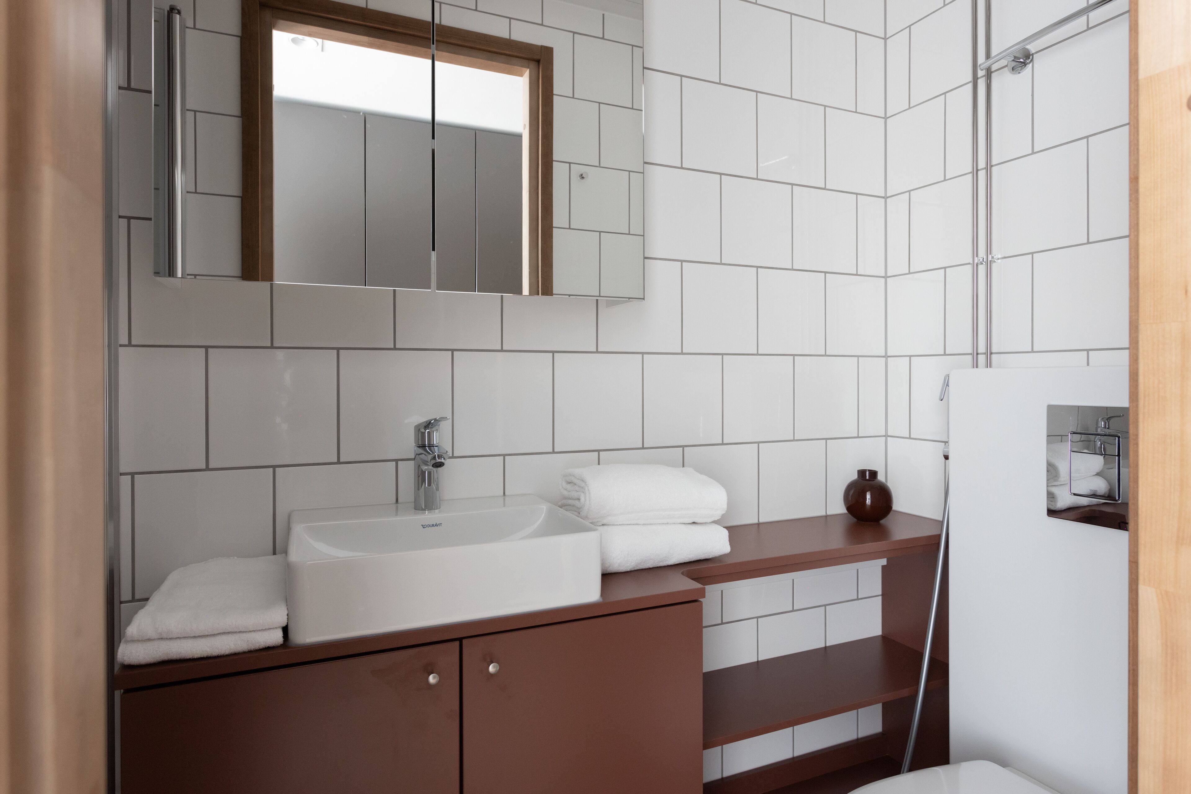 A modern bathroom with a white sink, a mirror, and a wooden vanity.