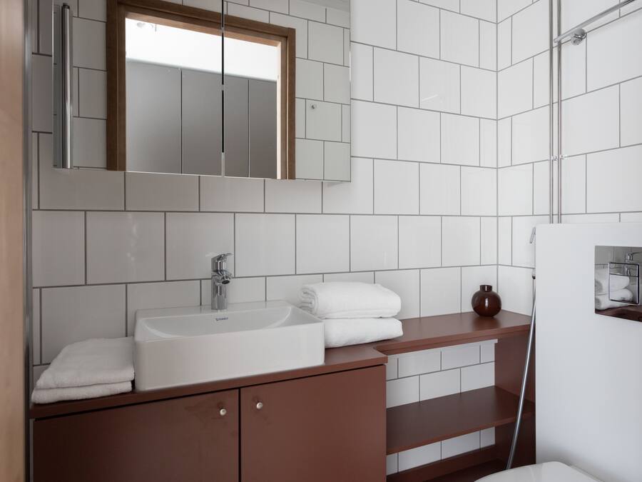 A modern bathroom with a white sink, a mirror, and a wooden vanity.