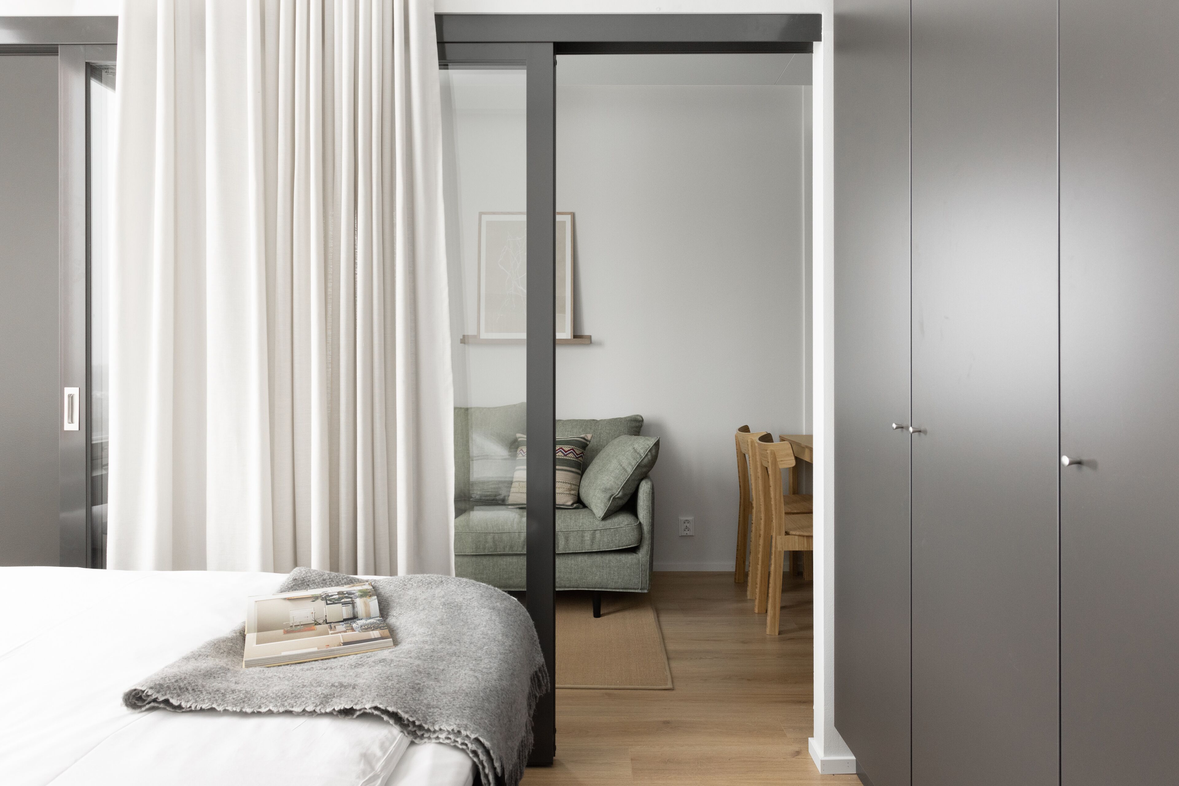 Un dormitorio moderno con cama, armario gris, sofá verde y mesa de comedor de madera.