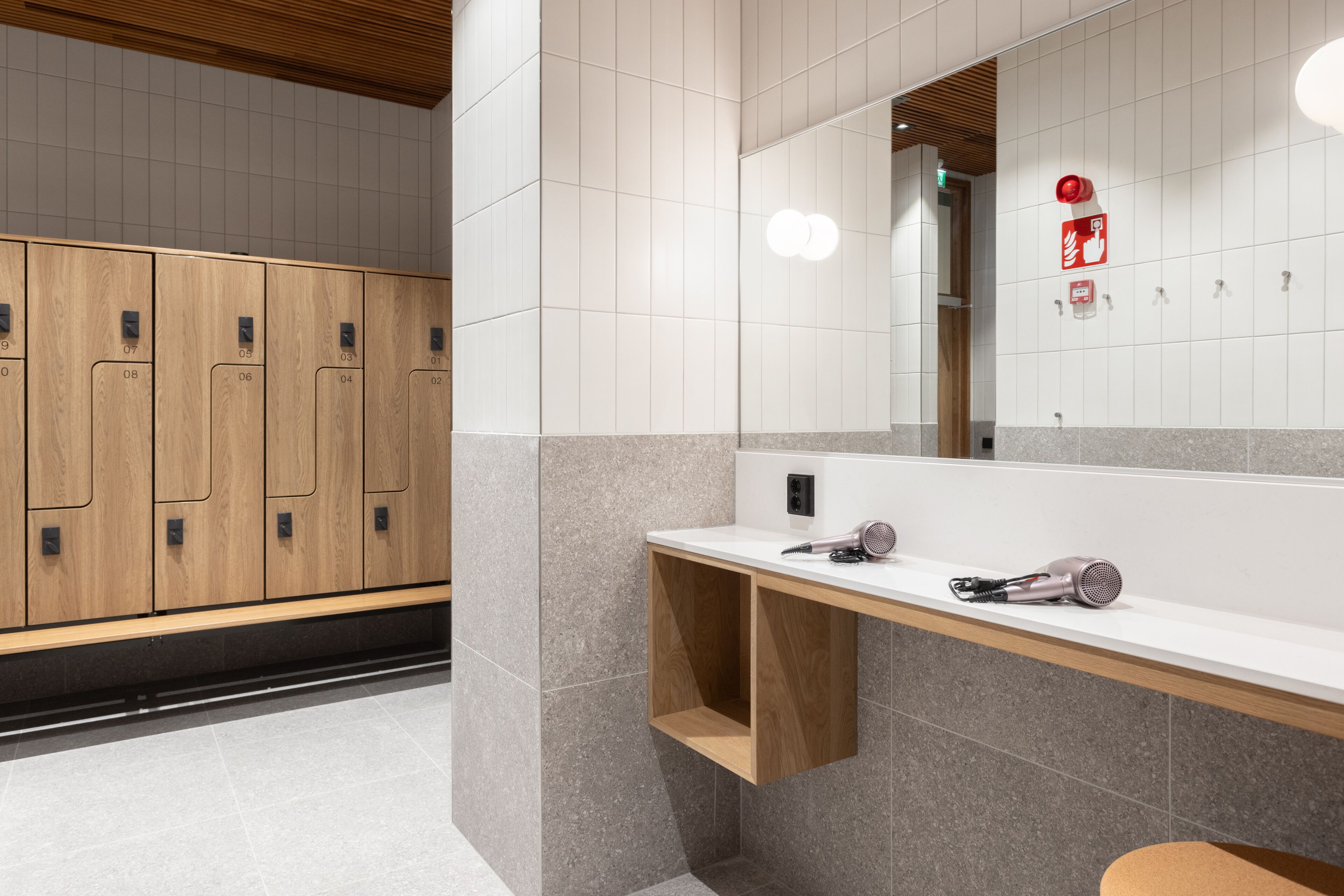 A modern bathroom with wooden lockers, a white sink, and a mirror.