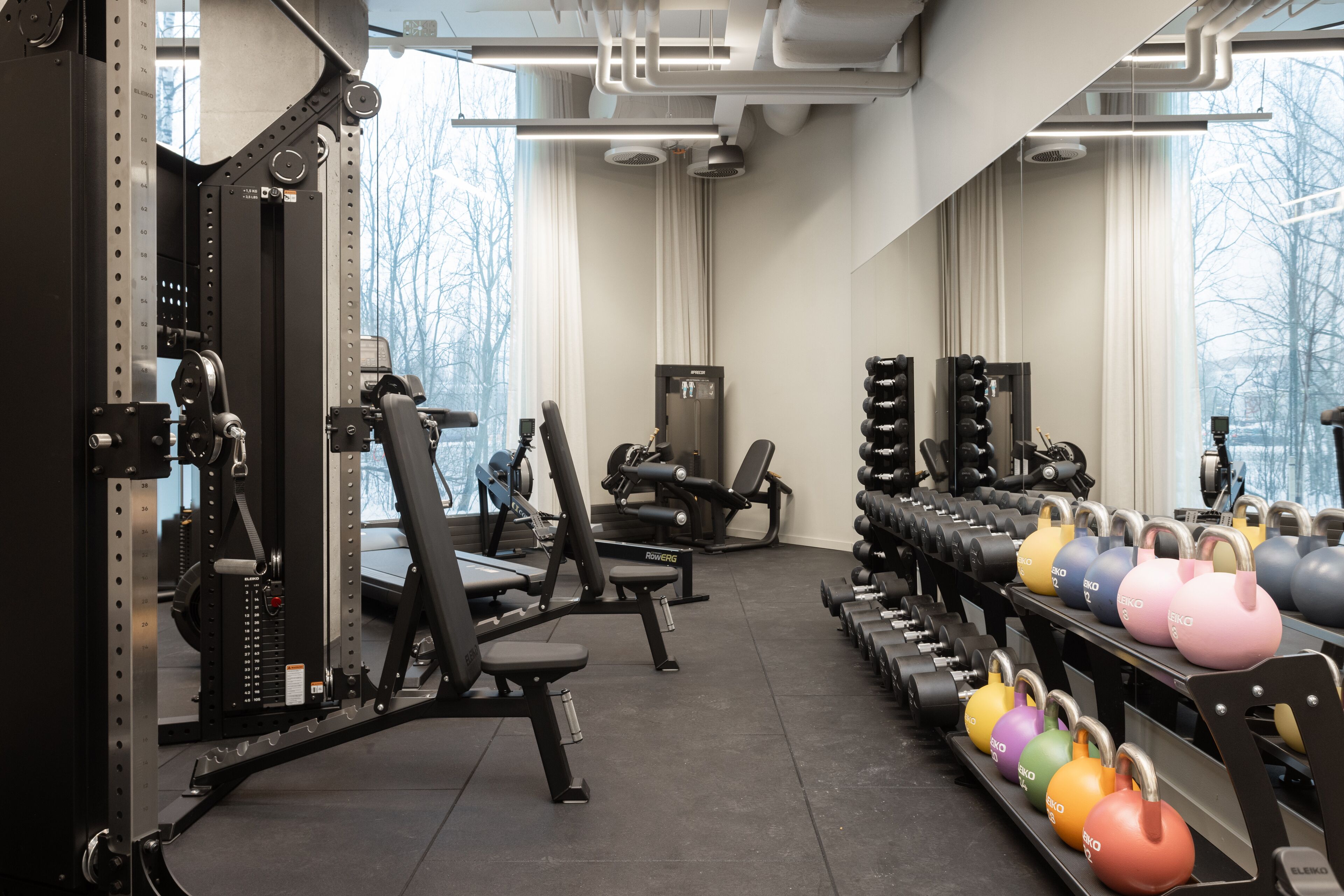 Un gimnasio con equipamiento de levantamiento de pesas, mancuernas y máquinas de ejercicio.