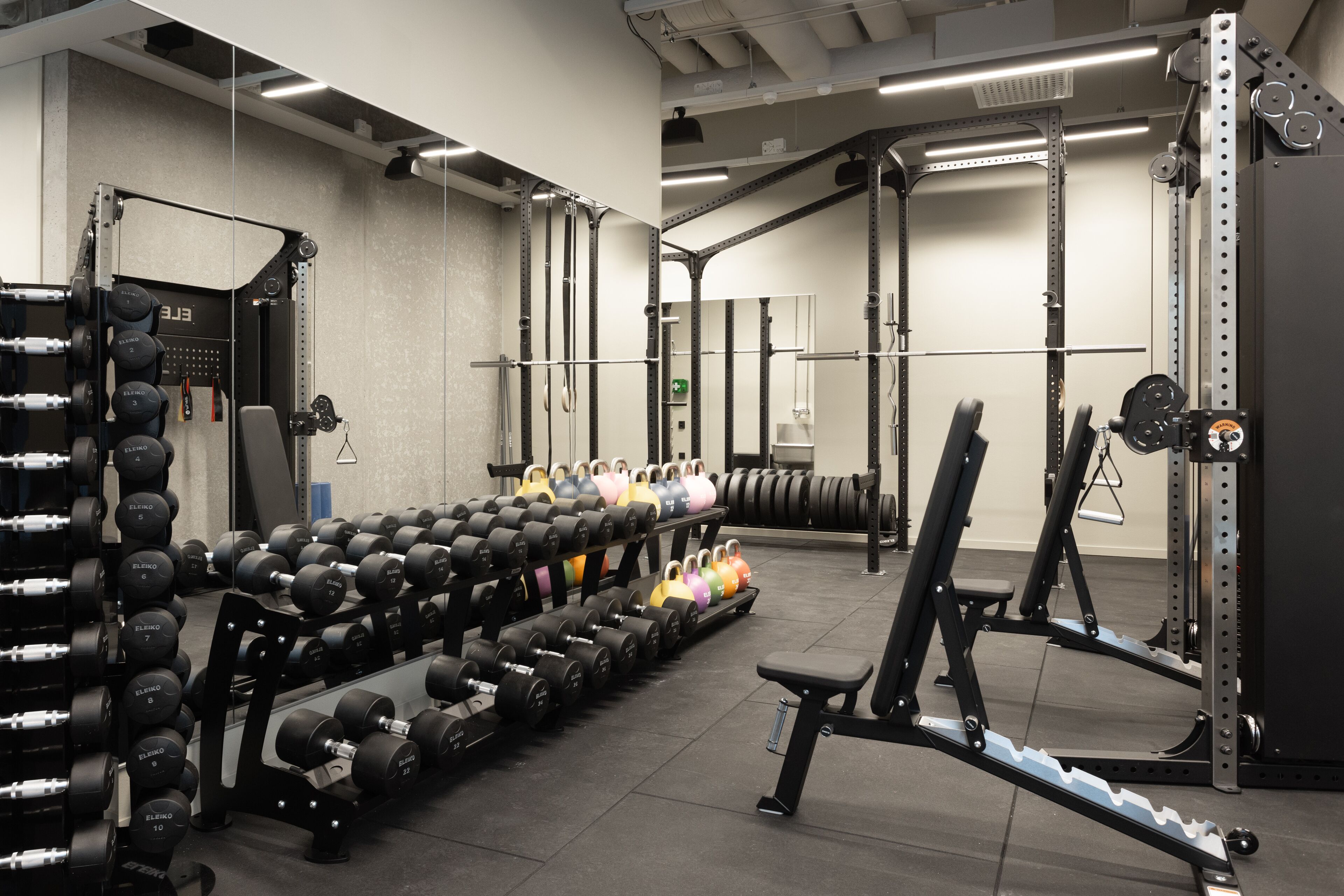 Ein Fitnessraum mit Gewichtstrainingsgeräten, darunter Kurzhanteln und ein Squat-Rack.