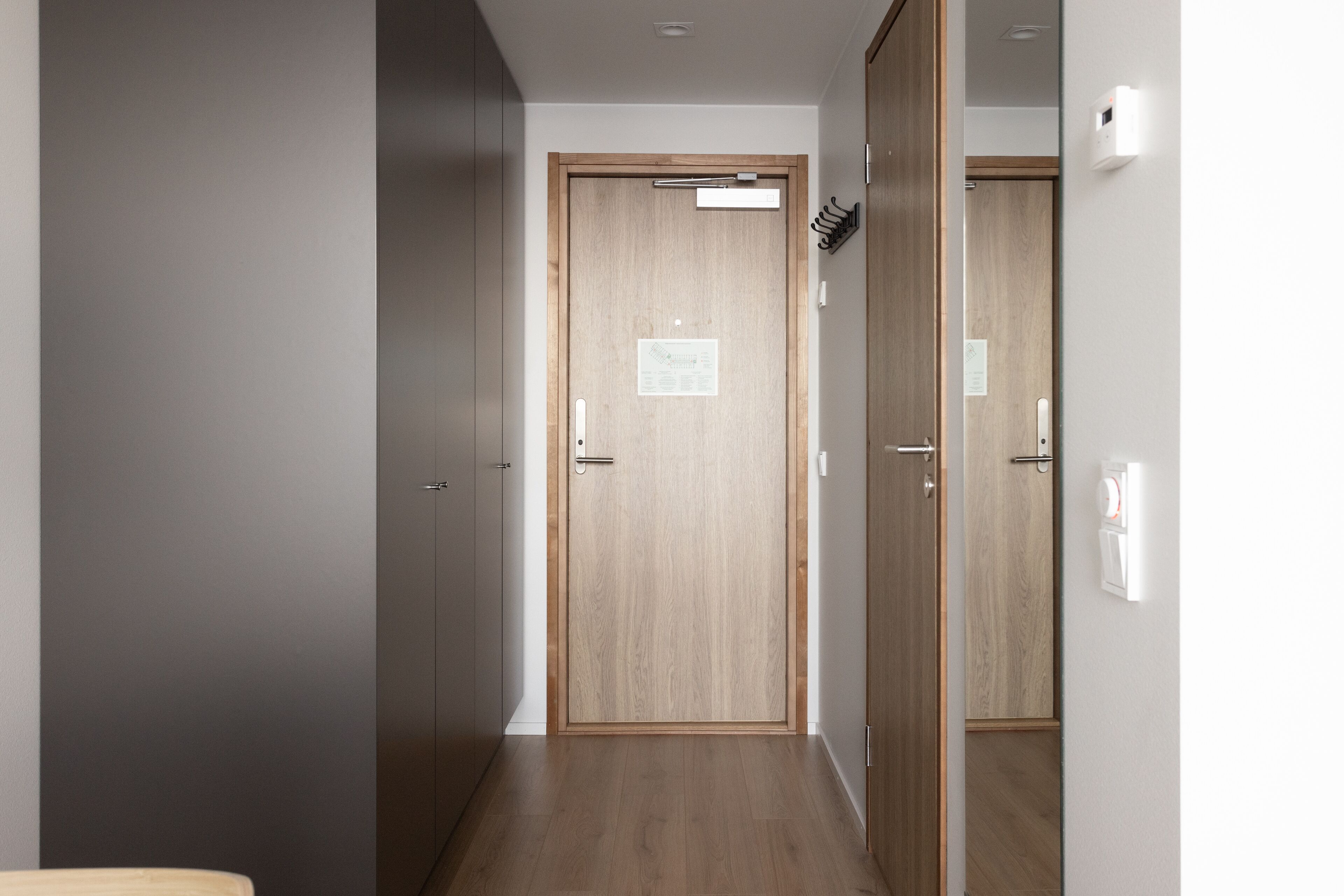 A hallway with a wooden door, a coat rack, and a light switch on the wall.